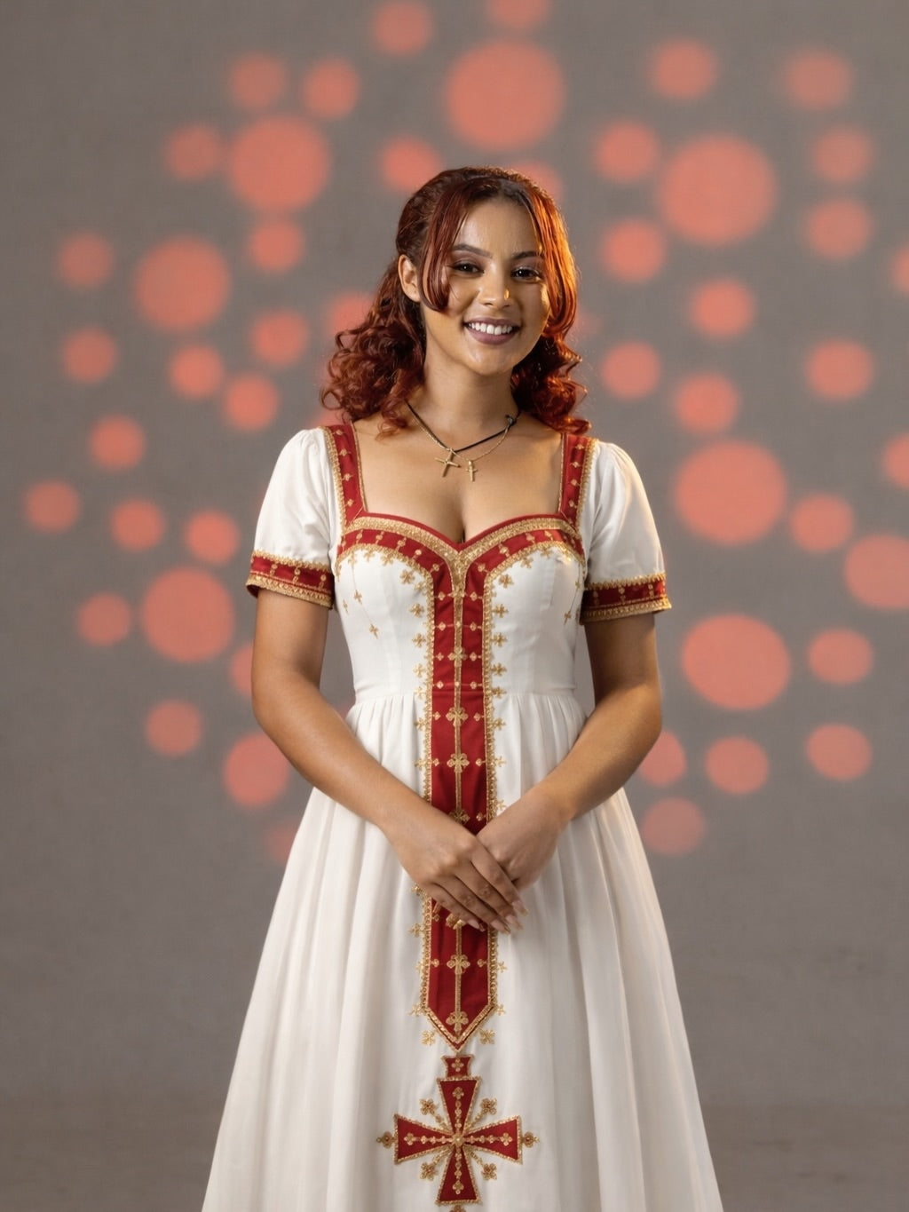 Woman wearing a white dress with red and gold embroidery against a polka dot background