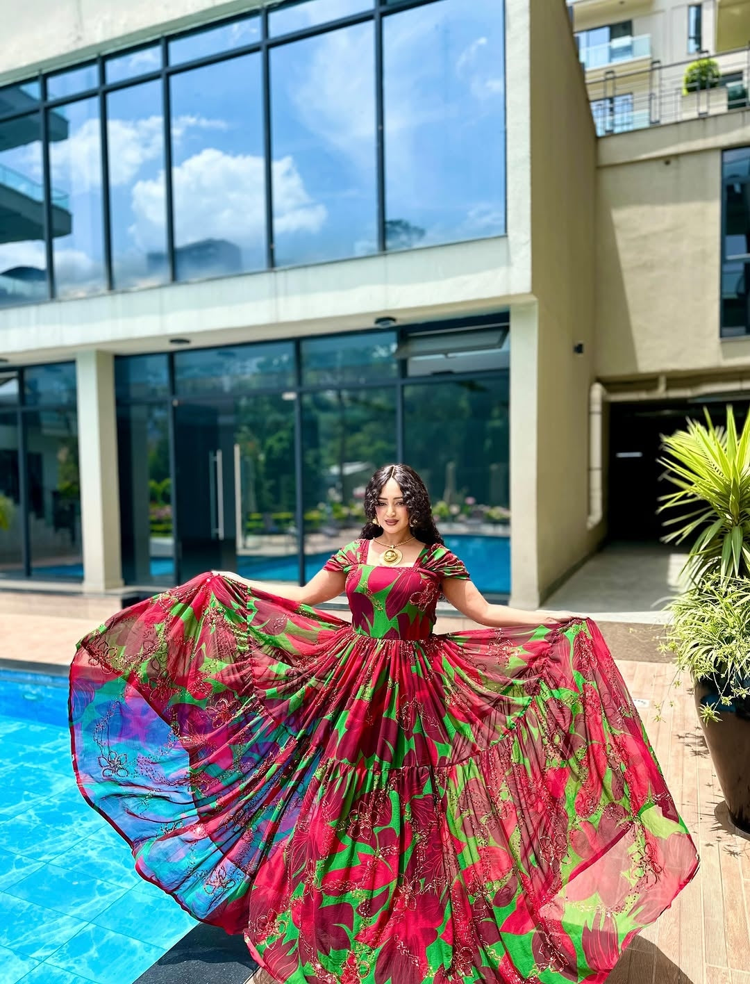 Woman in a colorful Habesha Chiffon  standing by a pool with a modern building in the background