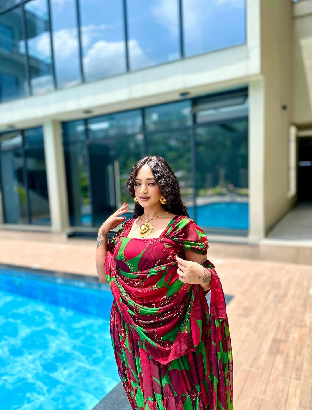 Woman in a red and green traditional Habesha Chiffon  standing by a pool.