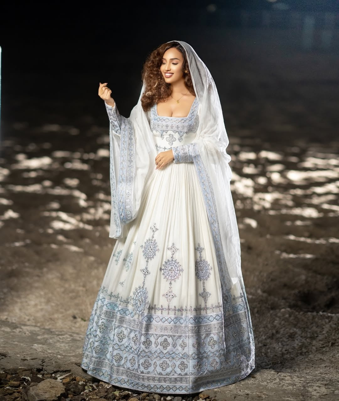 Woman in a white and blue habesha dress with a veil standing outdoors.
