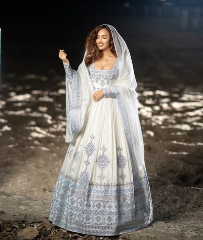Woman in a white and blue habesha dress with a veil standing outdoors.