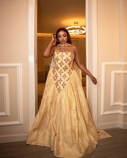 Woman in a gold evening habesha wedding dress with floral embroidery standing in a doorway.