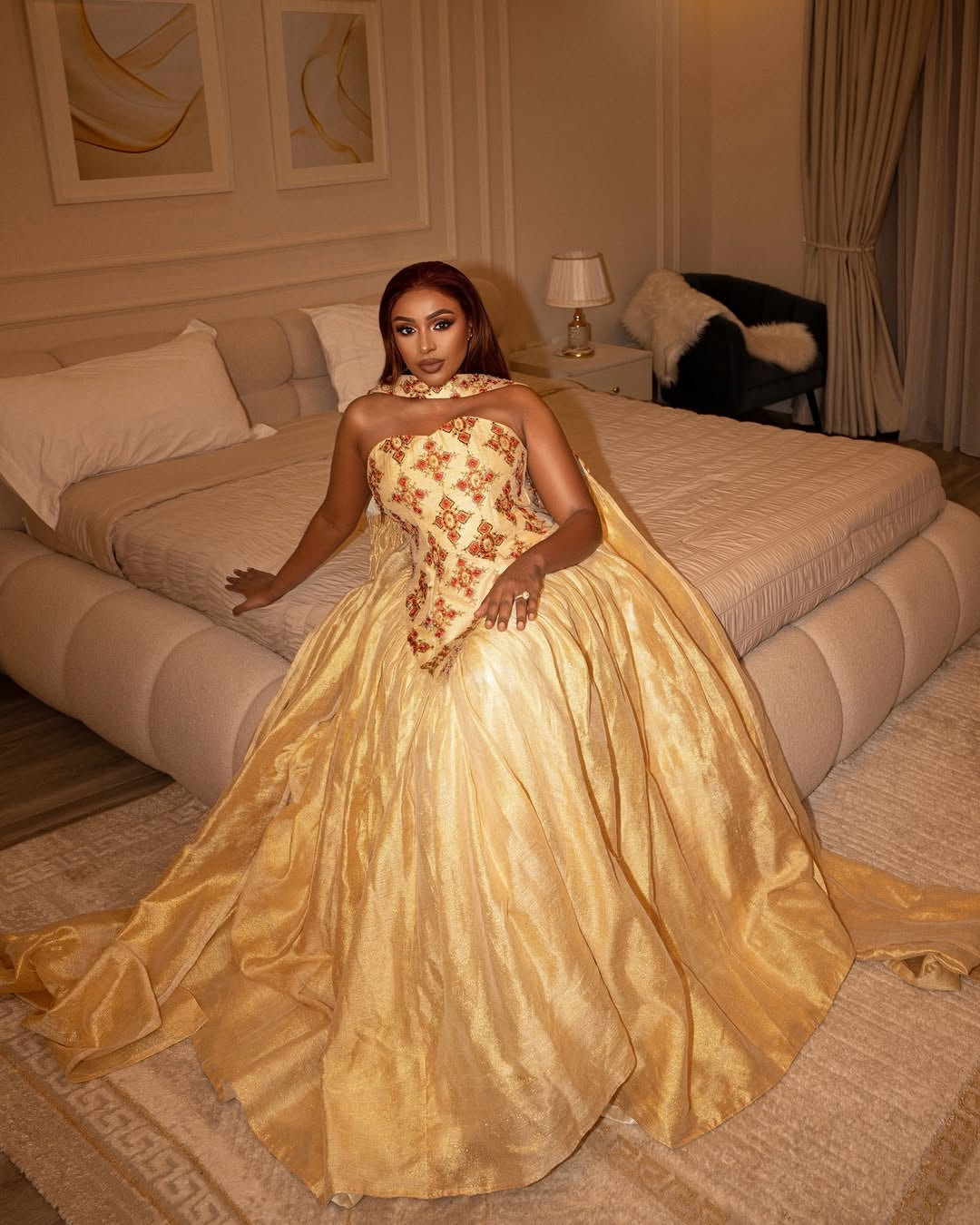 Woman in a gold and floral wedding  dress standing in a bedroom.