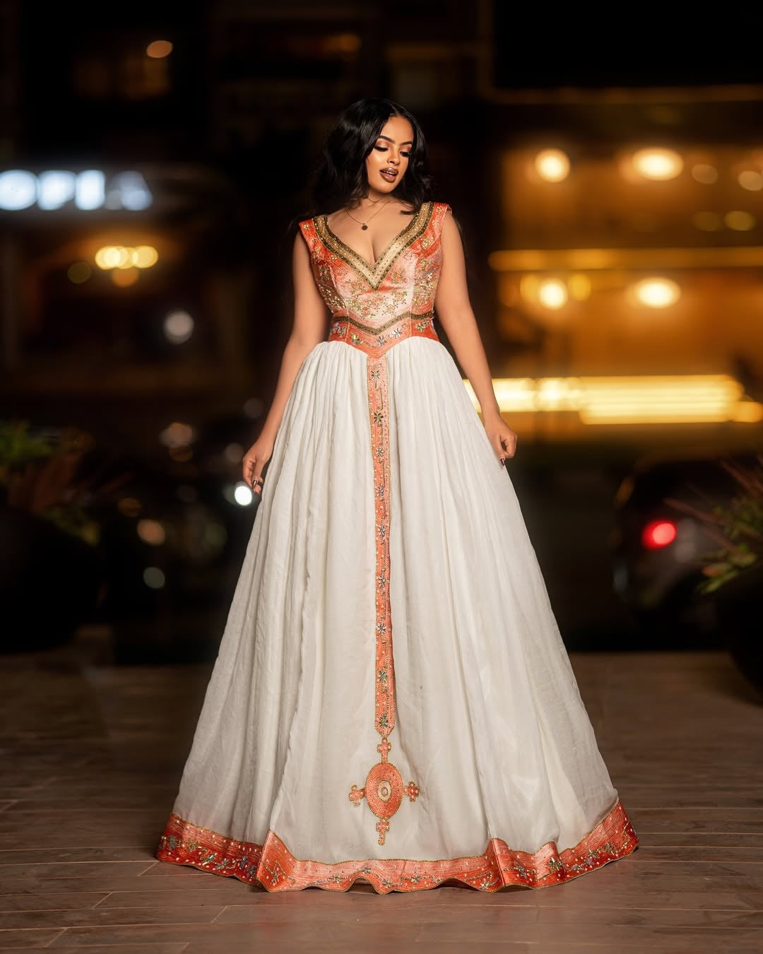 Woman in a white and orange traditional Ethiopian cultural dress  standing on a street at night.