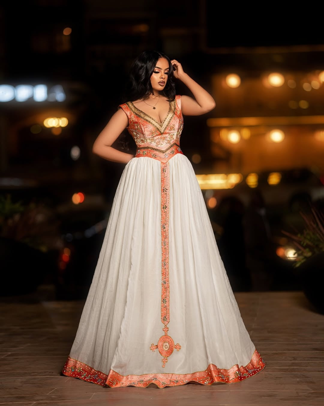 Woman in a white and orange embroidered Ethiopian cultural dress standing outdoors at night.