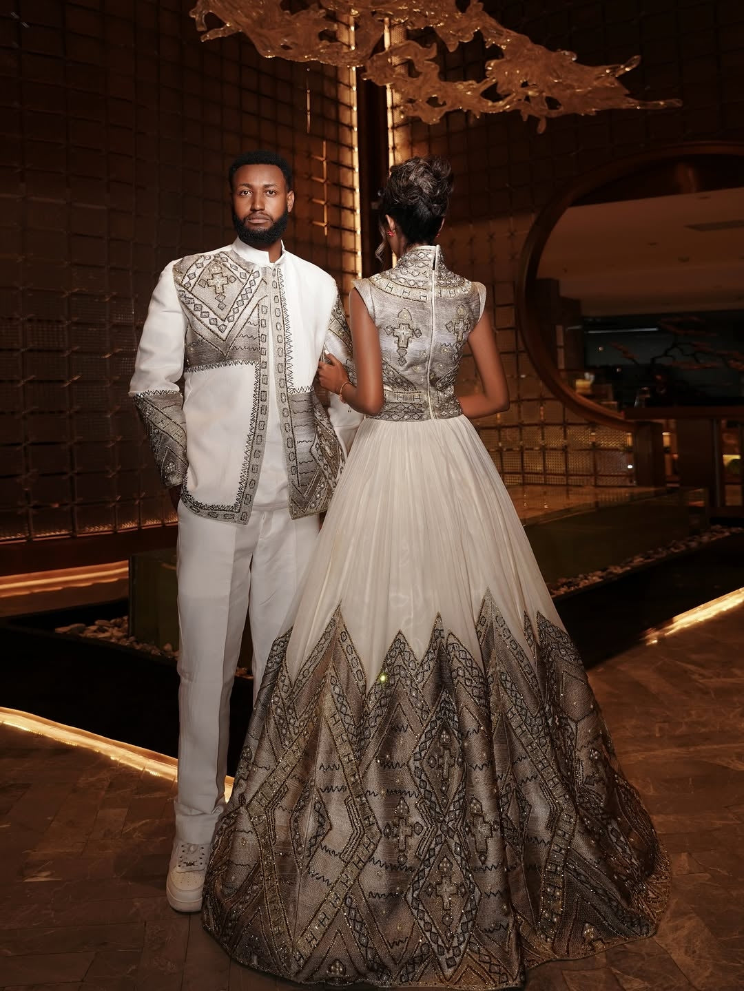 Man and woman in formal Ethiopian Matching Couple Set standing in a decorated indoor setting