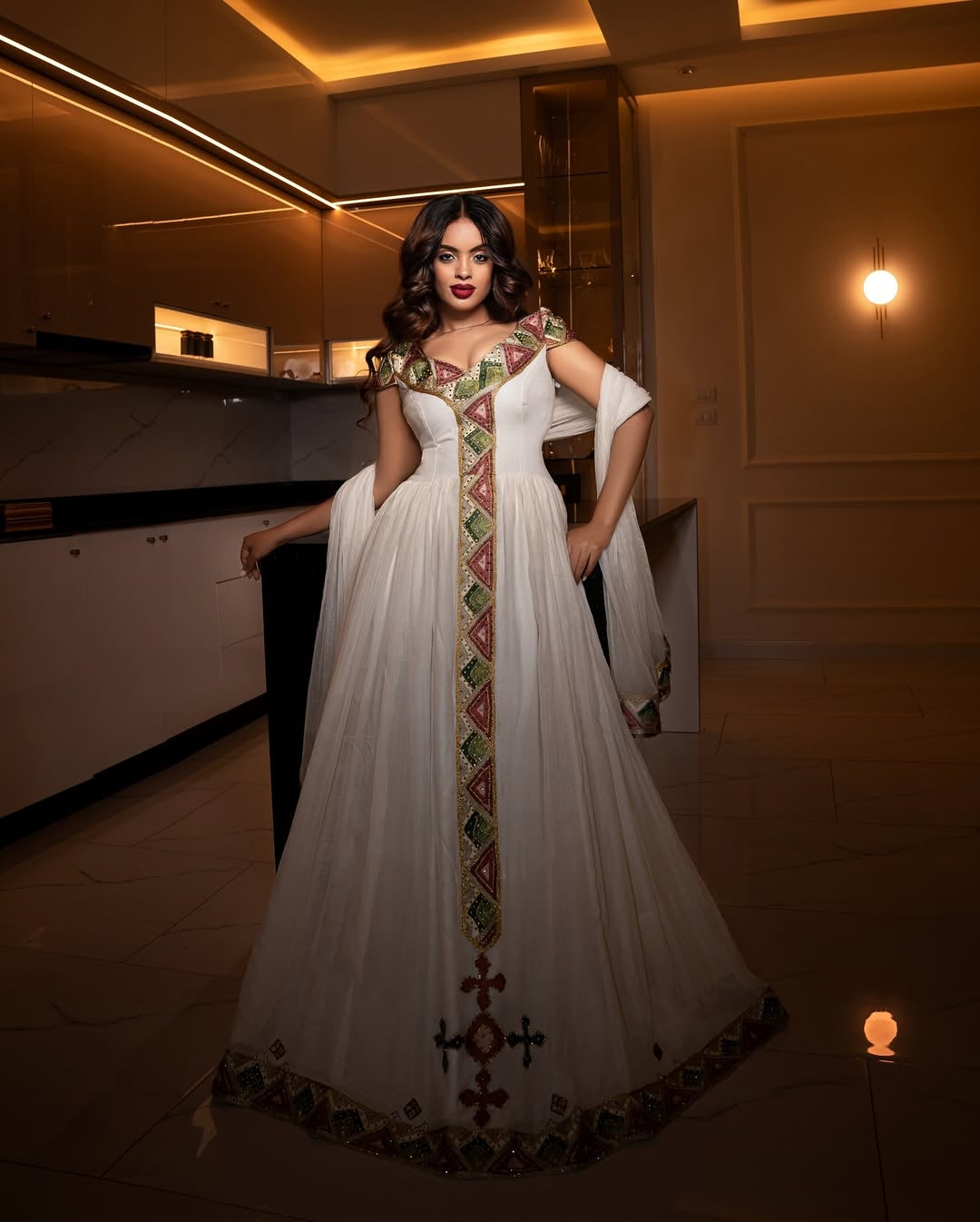 Woman wearing a white habesha dress with intricate patterns in an indoor setting