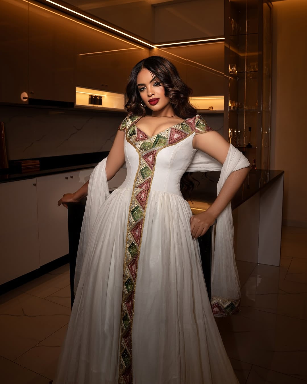 Woman in a white and patterned habesha dress standing in an indoor setting.