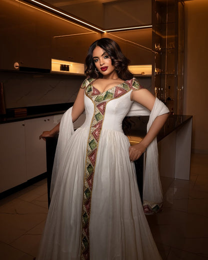 Woman in a white and patterned habesha dress standing in an indoor setting.