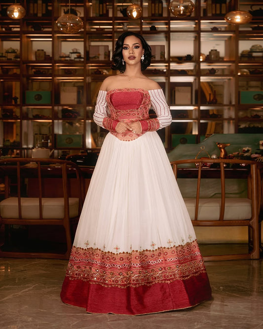 Woman wearing a white Ethiopian cultural dress with red patterned hem against a plain background