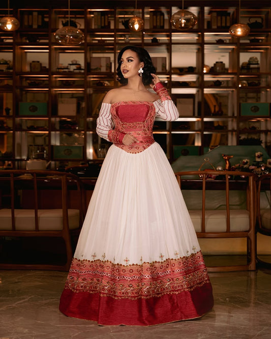 Woman wearing a white Ethiopian cultural dress with red patterned hem against a plain background