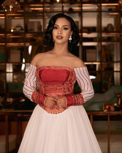 Woman wearing a white Ethiopian cultural dress with red patterned hem against a plain background