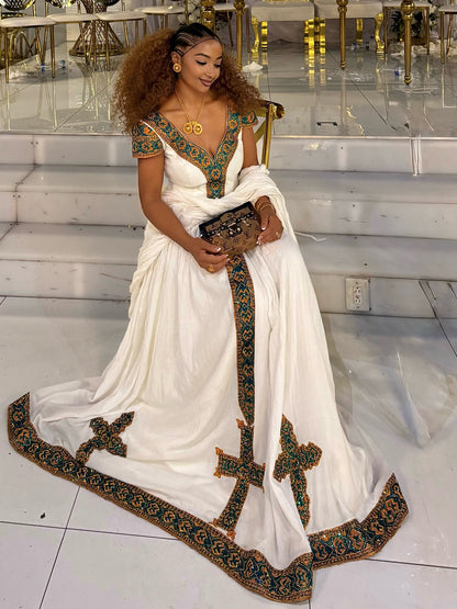 A woman wearing a white traditional Habesha Kemis with ornate green and gold embroidered borders, holding a small black clutch in a bright indoor setting with reflective tiled floors.