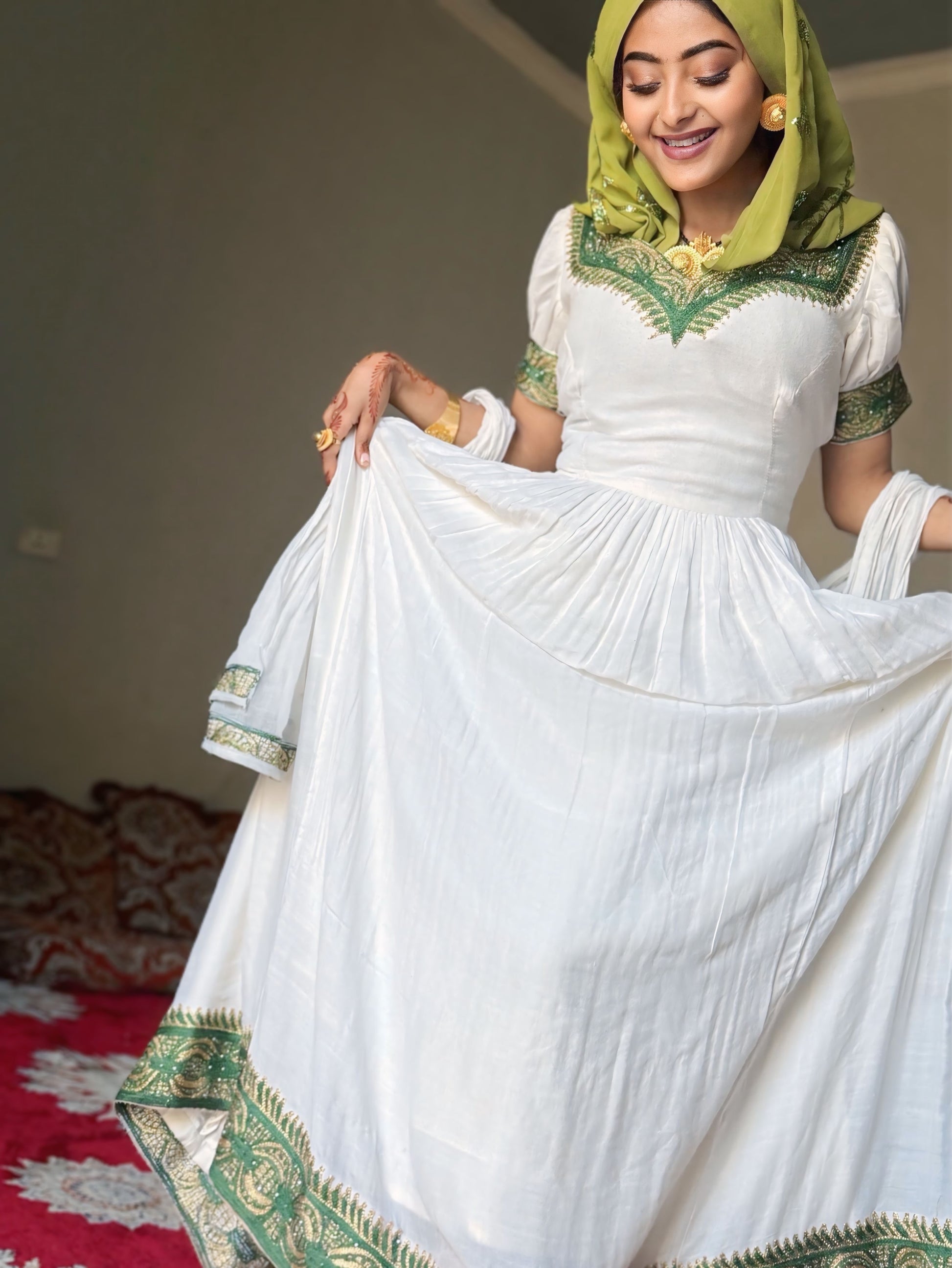 A woman wearing a white traditional  Habesha Dress  with green embroidered details and a matching green headscarf, holding out the skirt to show its full flow and decorative border.